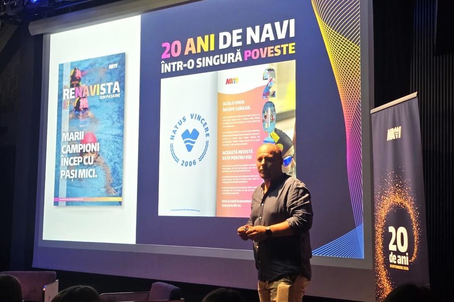 Cătălin Becheru prezetând revista pe care au tipărit-o pentru această aniversare Clubul NAVI, unde David Popovici l-a întâlnit pe Adrian Rădulescu, a sărbătorit douăzeci de ani de la înființare într-un cadru neobișnuit în care s-au rememorat începuturile grele, performanțele și aspirațiile