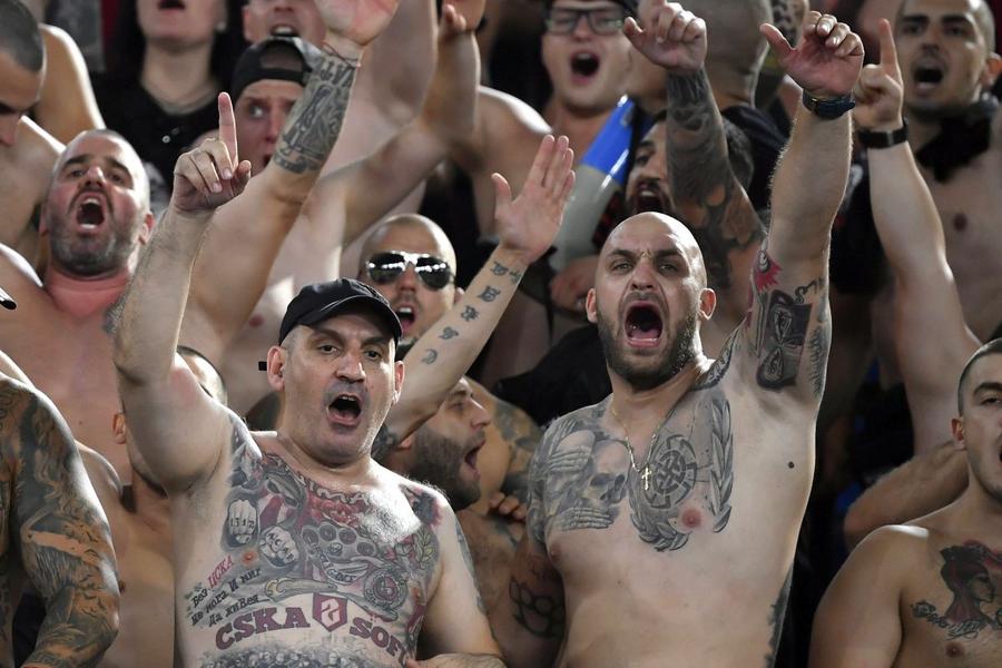 Ultrași ai lui CSKA Sofia, unul dintre ei cu o svastică tatuată pe piept, cântă în timpul duelului cu AS Roma, din 2021, în grupele Conference. Foto: Imago Images Cum s-a rupt Steaua Bulgariei în două echipe acum rivale » O luptă dramatică pentru putere, bani și identitate la CSKA Sofia: lanț uman de ultrași, oraș sub „lacăt”, amenințări