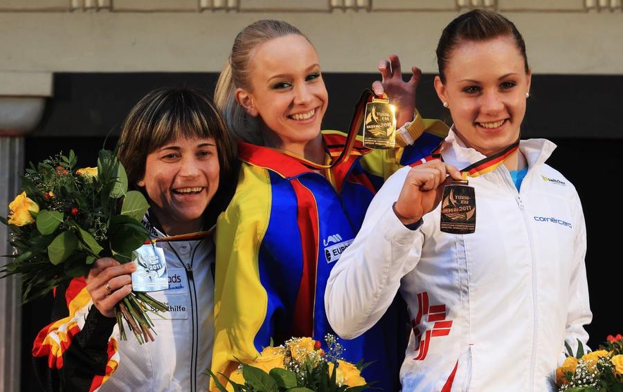 Oksana Chusovitina, pe podium lângă românca Sandra Izbașa, în anul 2011 Foto: Guliver / Getty Images Oksana Chusovitina, sportiva care la 50 de ani vrea să prindă a noua ei Olimpiadă: „Gimnastica mi-a salvat fiul din ghearele cancerului”