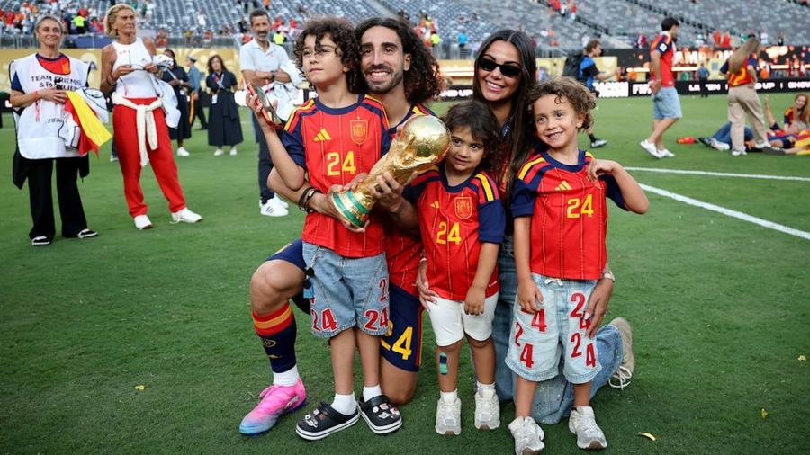 Familia Cucurella sărbătorește titlul mondial. Mateo (stânga) ține un smartphone într-o mână, iar cealaltă pe trofeu De ce Marc Cucurella nu se tunde scurt niciodată