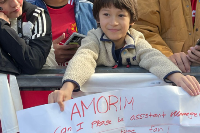 Jovem adepto do Manchester United segura um cartaz com um pedido a Ruben Amorim: «Posso ser adjunto do Man. United?»