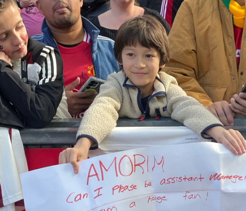 Jovem adepto do Manchester United segura um cartaz com um pedido a Ruben Amorim: «Posso ser adjunto do Man. United?»