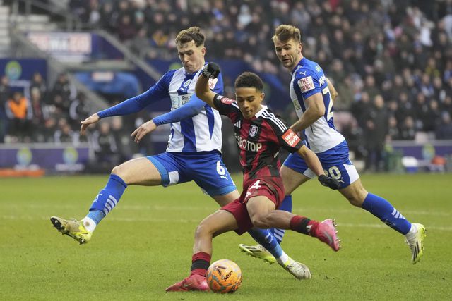 Joshua King remata perante a pressão de um defesa dos Latics