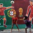Crianças brincam com uma bola em Calcutá, na Índia, em frente a mural com as figuras de Cristiano Ronaldo e João Cancelo