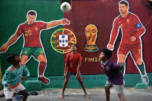 Crianças brincam com uma bola em Calcutá, na Índia, em frente a mural com as figuras de Cristiano Ronaldo e João Cancelo