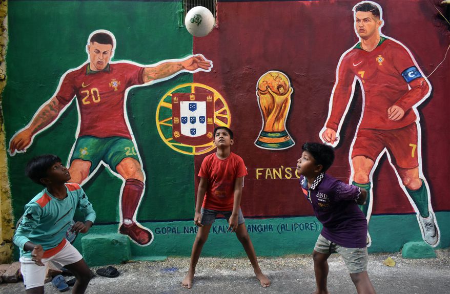 Crianças brincam com uma bola em Calcutá, na Índia, em frente a mural com as figuras de Cristiano Ronaldo e João Cancelo