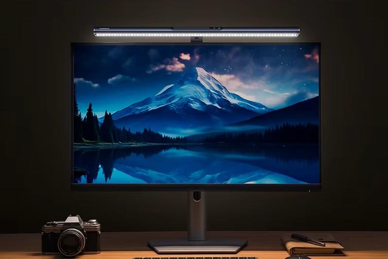 Luz magnética de ecrã Baseus i-wok3 montada num monitor. A luz ilumina uma mesa de trabalho em madeira com teclado, rato, caderno e câmara.