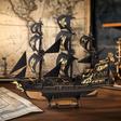 Modelo 3D de um barco. A maquete está apoiada sobre uma mesa de madeira, com mapas antigos compondo o cenário ao fundo.