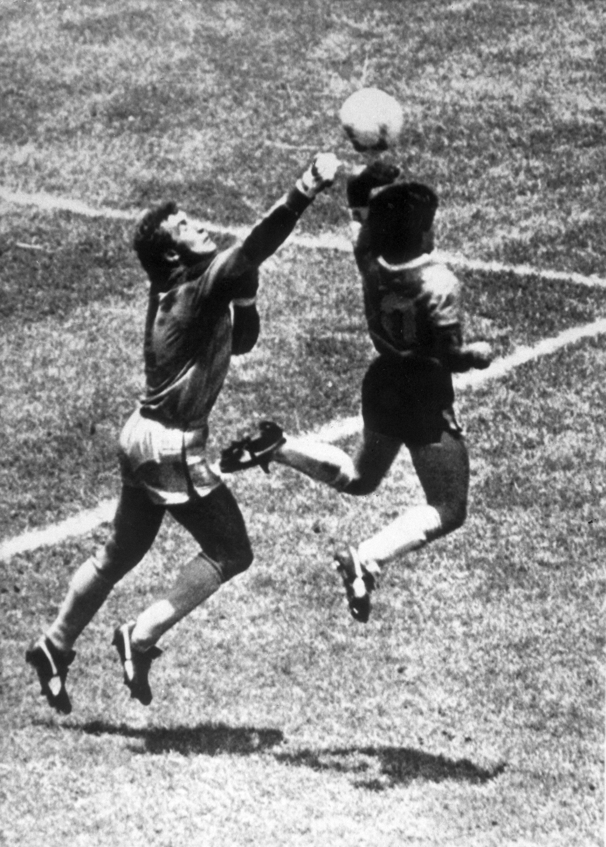 Momento em que Maradona toca a bola com a mão, numa disputa com o guarda-redes Shilton, abrindo o marcador no jogo entre Argentina e Inglaterra, dos quartos de final do Mundial 1986 - Foto: IMAGO