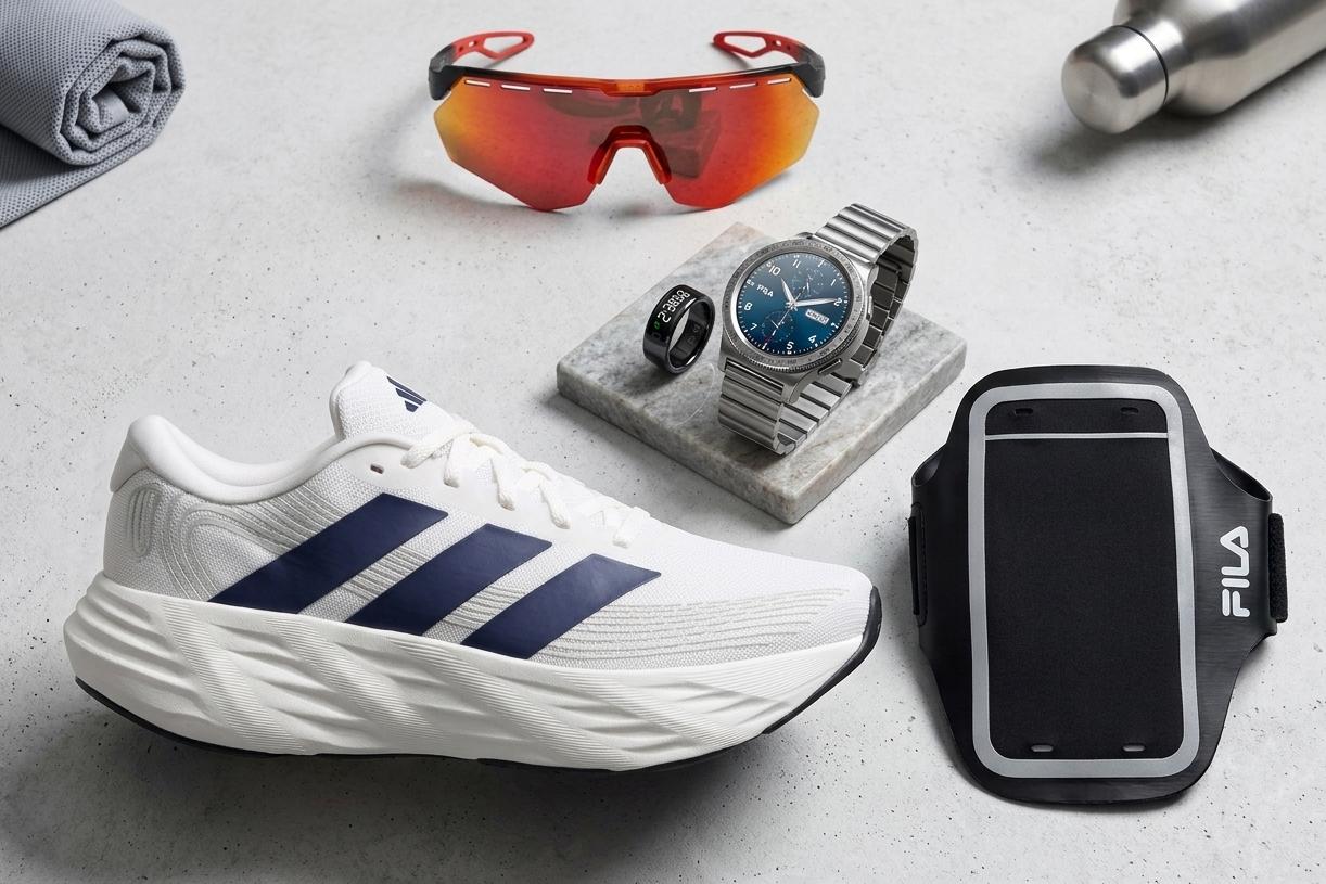 Fotografia vista de cima com equipamento de corrida sobre fundo cinzento: um ténis Adidas branco, óculos de sol vermelhos, relógio, anel inteligente e braçadeira.