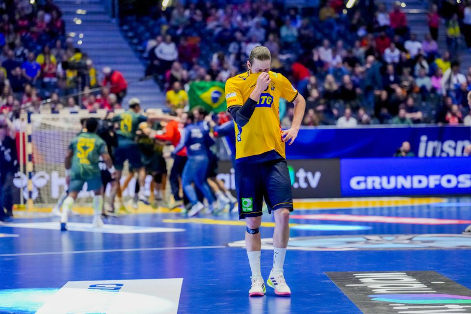 Jogador sueco desolado, com os brasileiros ao fundo a celebrar a vitória no jogo do Mundial de andebol