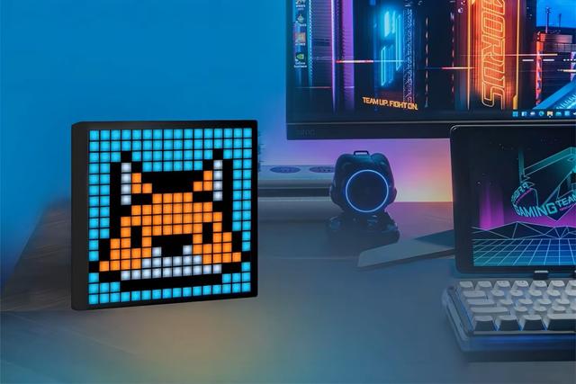 Um ecrã digital sobre uma secretária exibe uma raposa em pixel art. Ao fundo, num ambiente iluminado, um monitor, um pequeno dispositivo com luz azul, um tablet e um teclado.
