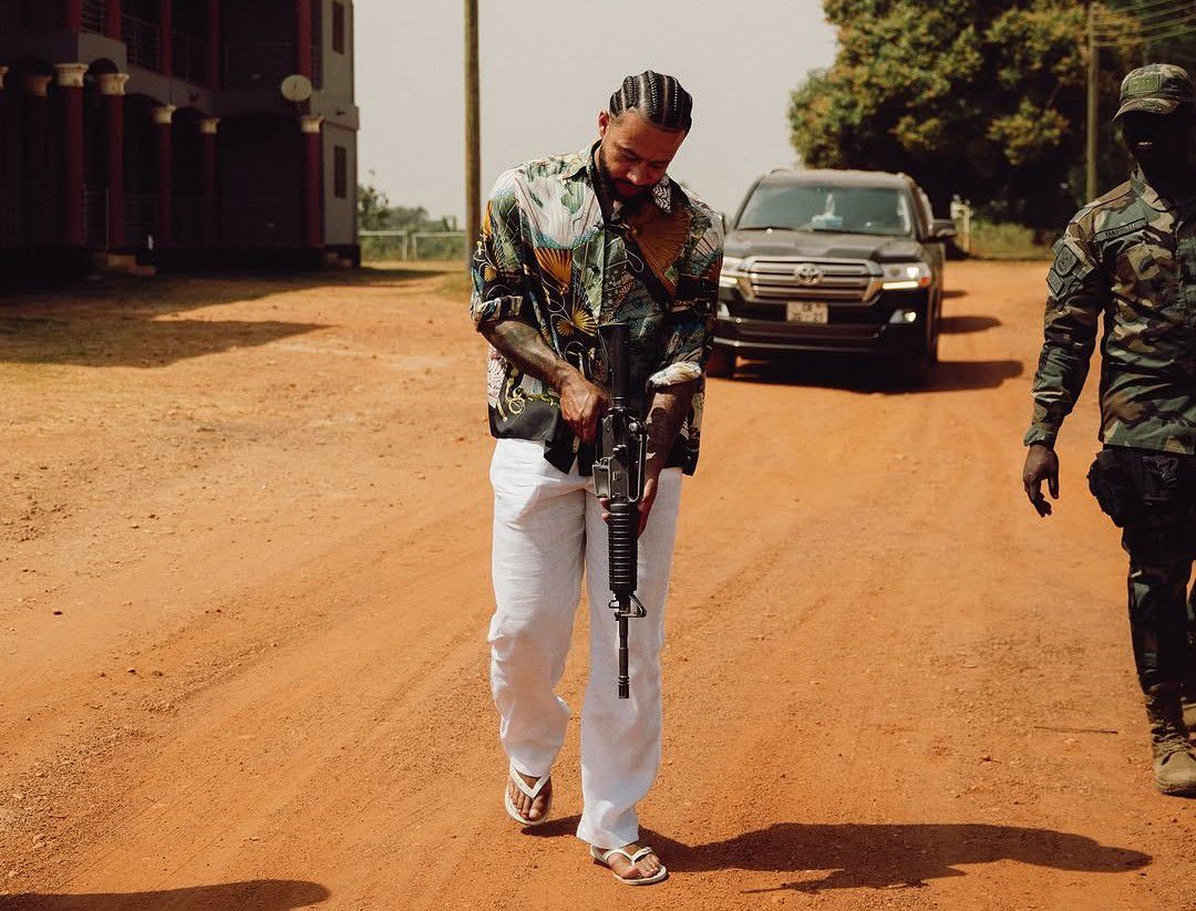 Memphis Depay segura uma espingarda, acompanhado de um militar