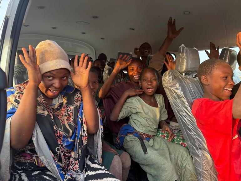 Rescued school children and staff from St Mary's Catholic School Papiri smiling and waving inside a vehicle after release.