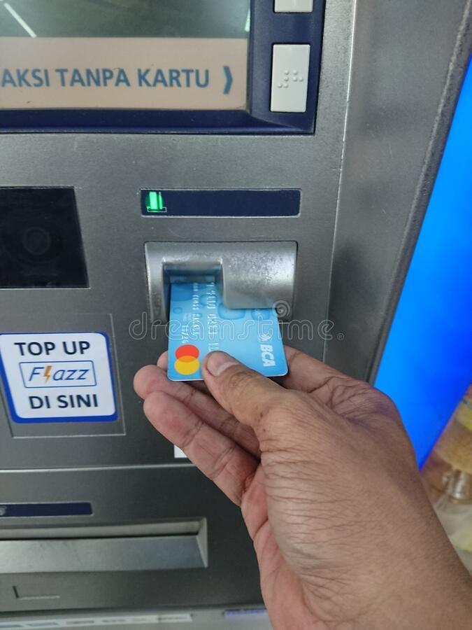 A customer inserting a debit card into an ATM machine to withdraw cash during a bank transition phase.