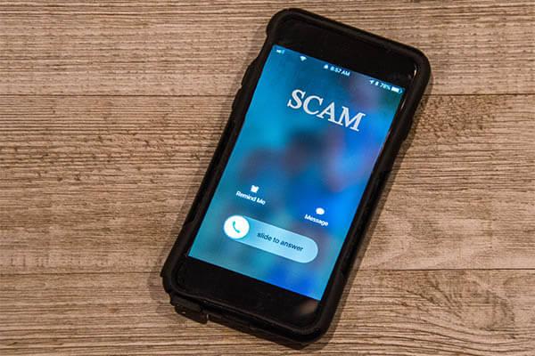 A smartphone lying on a wooden table displaying an incoming fraudulent scam call.