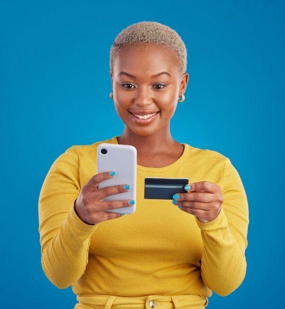 A smiling Nigerian woman holding a debit card and checking her mobile banking app on a smartphone.
