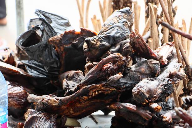 A market display of smoked and dried African bushmeat, showing the dark, charred textures of wildlife meat stacked together next to wooden sticks.