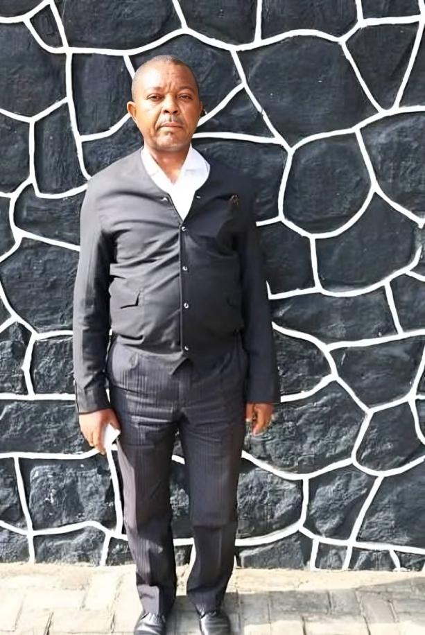 Full-length photo of 55-year-old John Nwawuto Anoruo standing against a black-and-white stone wall.