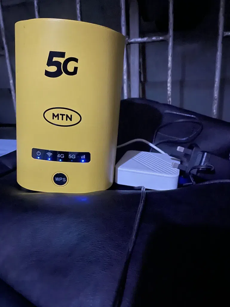 A bright yellow MTN 5G Broadband Router with blue LED indicator lights turned on, sitting on a dark surface.