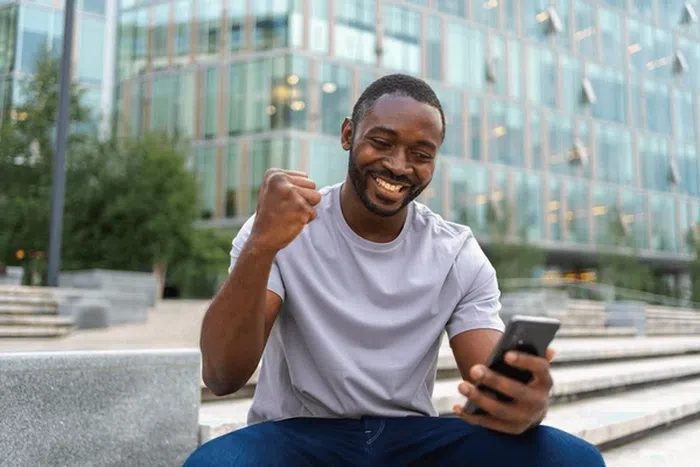 Young Nigerian smiling while using cheap MTN, Glo, and Airtel data on a smartphone