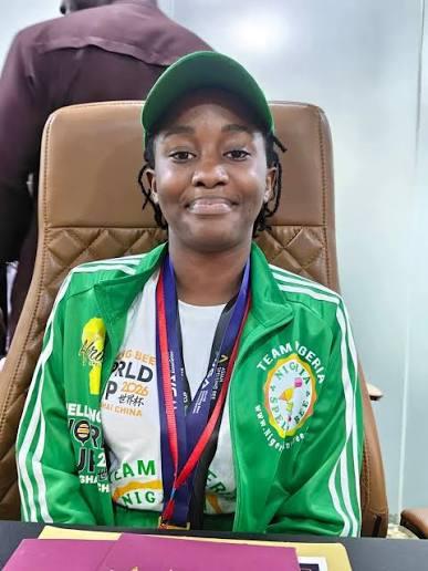 Portrait of World Spelling Bee winner Damilola Adeolu seated in a green Team Nigeria tracksuit, cap, and gold medal.