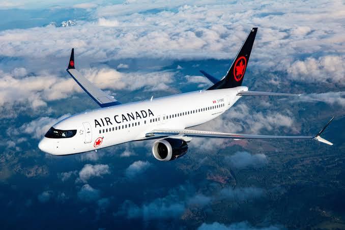 An Air Canada commercial passenger aircraft flying through blue skies above a sea of white clouds.
