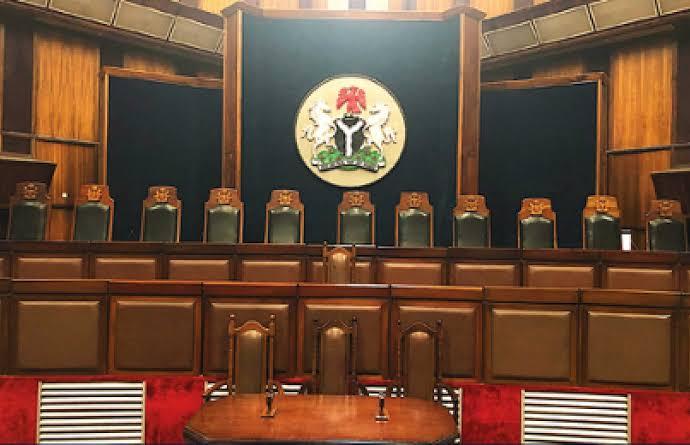 Interior view of the empty judges' bench and desks inside the Federal High Court in Abuja, showing the Nigerian coat of arms.