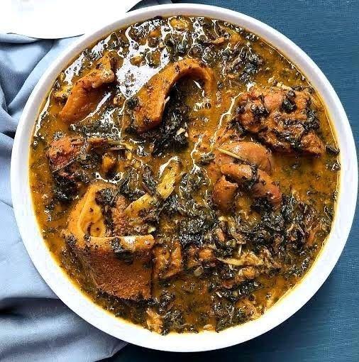 A white bowl of thick bitter leaf soup with tender meat pieces.