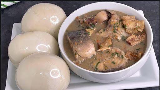 A bowl of light-coloured Ofe Nsala soup with catfish, served next to pounded yam.
