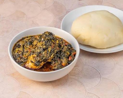 A bowl of dark green Ofe Owerri soup with meat, paired with a white ball of fufu.