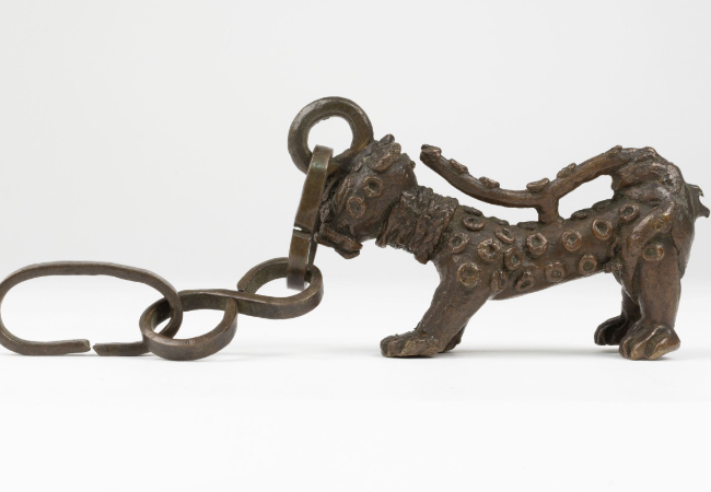 Brass leopard with raised spots, attached by the head to a chain.