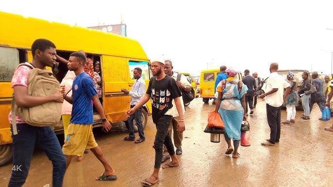 Nigerian youths navigating a busy Lagos street near yellow commercial buses (Danfo).