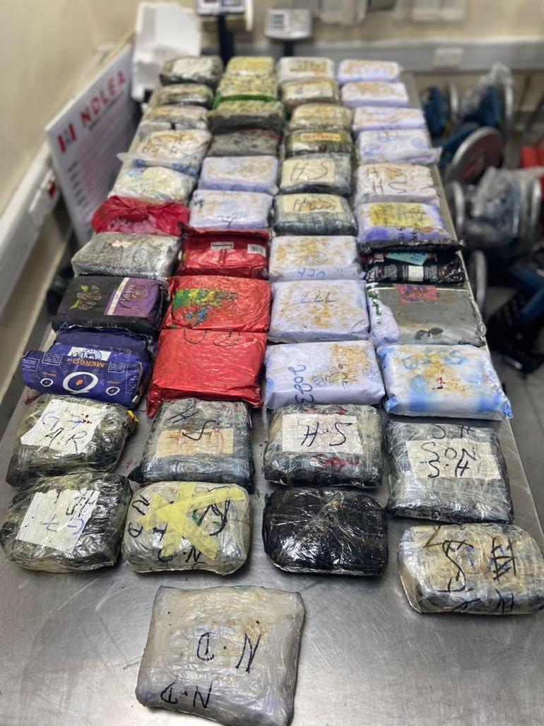 Dozens of tightly wrapped parcels of suspected illicit drugs arranged on an examination table.