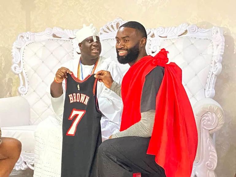 NBA champion Jaylen Brown kneeling to present his black number 7 basketball jersey to the seated Ooni of Ife, Oba Adeyeye Ogunwusi, during a cultural visit to Ile-Ife.
