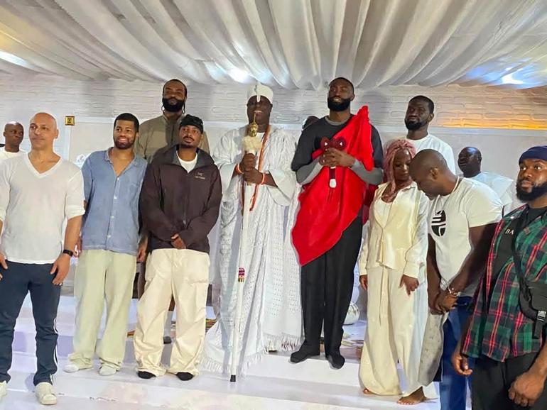 Group photo of NBA player Jaylen Brown, his companions, and the Ooni of Ife posing together on a white platform inside the Ile-Ife royal palace.