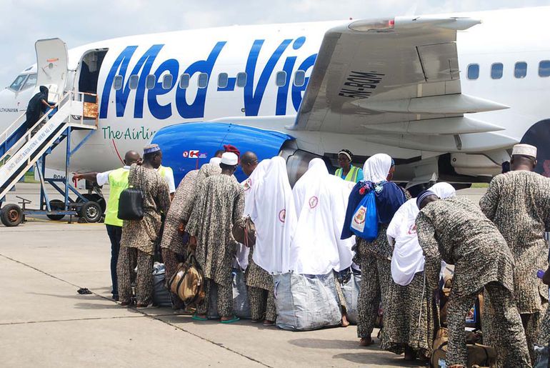Group of Nigerian Muslim pilgrims in traditional patterned uniforms boarding a Med-View Airline flight for Hajj.