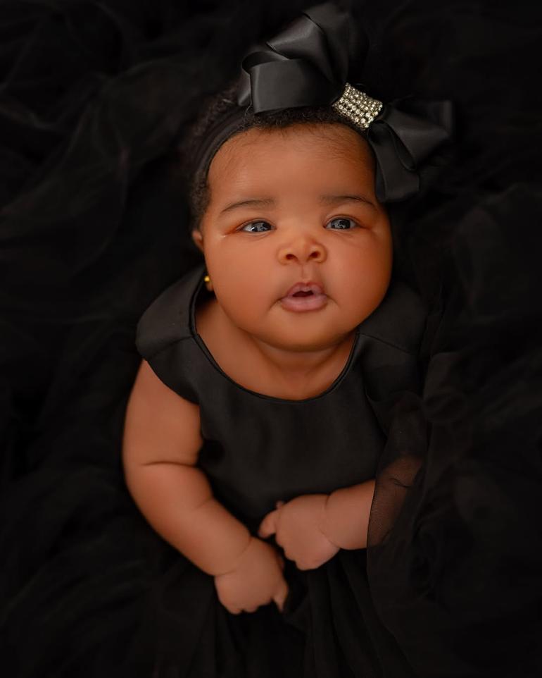 Close-up face reveal photo of Veekee James and Femi Atere’s baby daughter, Eliana Atere, wearing a luxury black dress and matching satin bow headband.