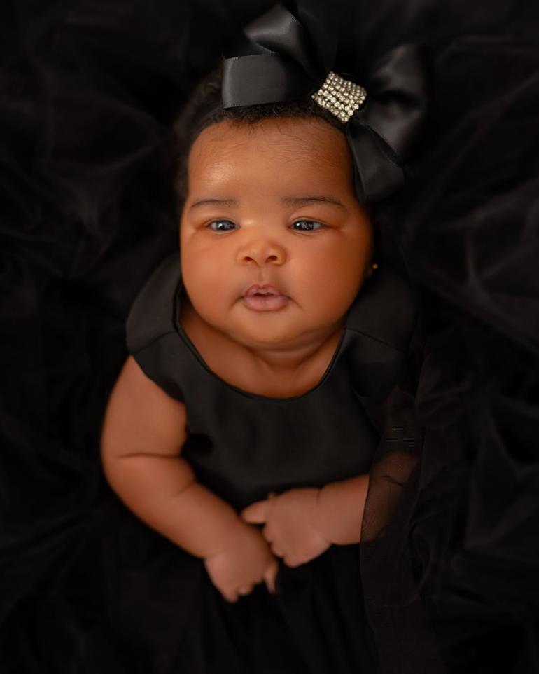 Close-up face reveal photo of Veekee James and Femi Atere’s baby daughter, Eliana Atere, wearing a luxury black dress and matching satin bow headband.