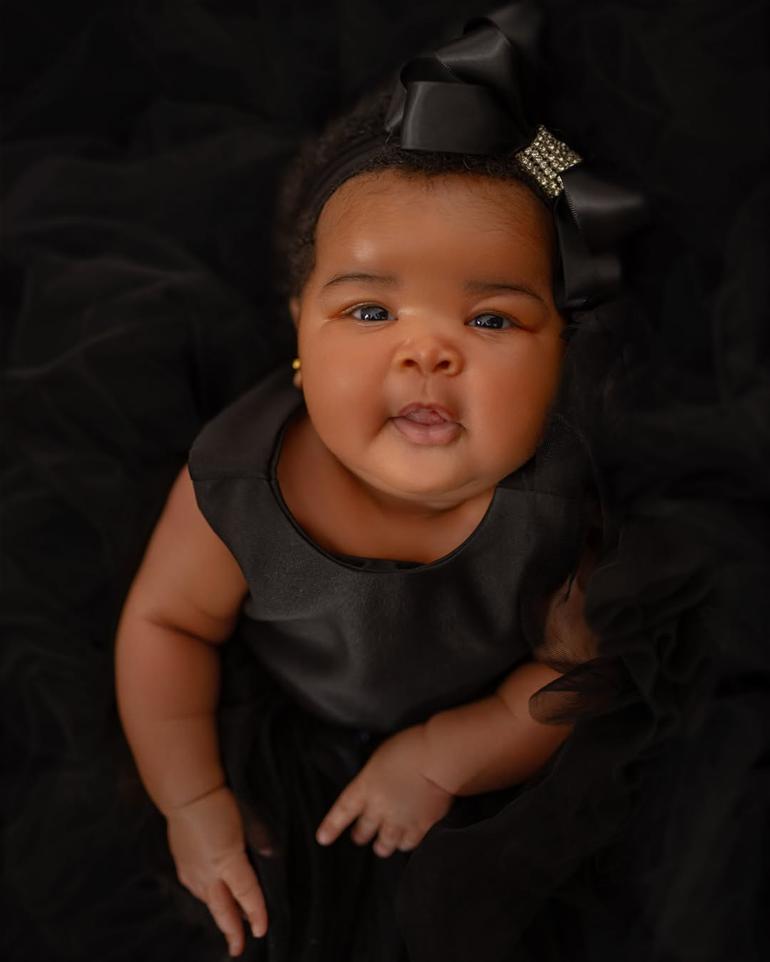 Close-up face reveal photo of Veekee James and Femi Atere’s baby daughter, Eliana Atere, wearing a luxury black dress and matching satin bow headband.