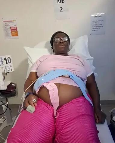 The expectant mother rests in a hospital bed with fetal monitoring belts strapped across her bare pregnant belly.