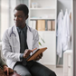 A male Nigerian doctor in a white coat showing medical data on a tablet to a female patient in a professional hospital setting.