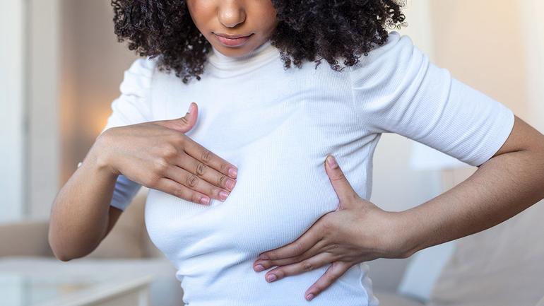 A Black woman performing a breast self-examination at home to check for unusual lumps or skin changes.