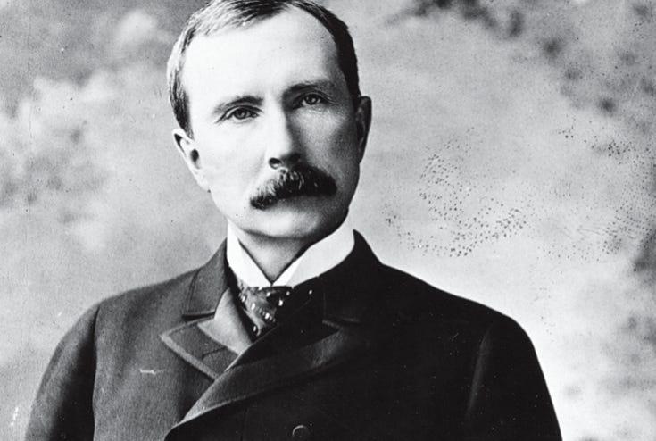A black and white historical portrait of John D. Rockefeller wearing a dark suit and a tie.