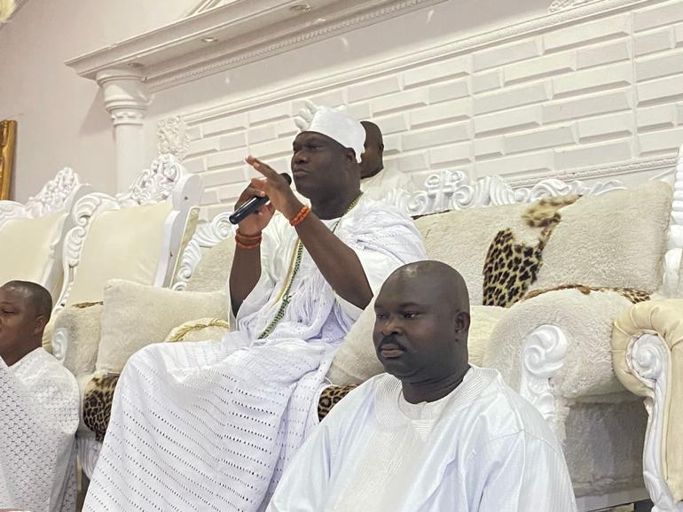 The Ooni of Ife, Oba Adeyeye Ogunwusi, wearing traditional white attire and addressing an audience with a microphone.