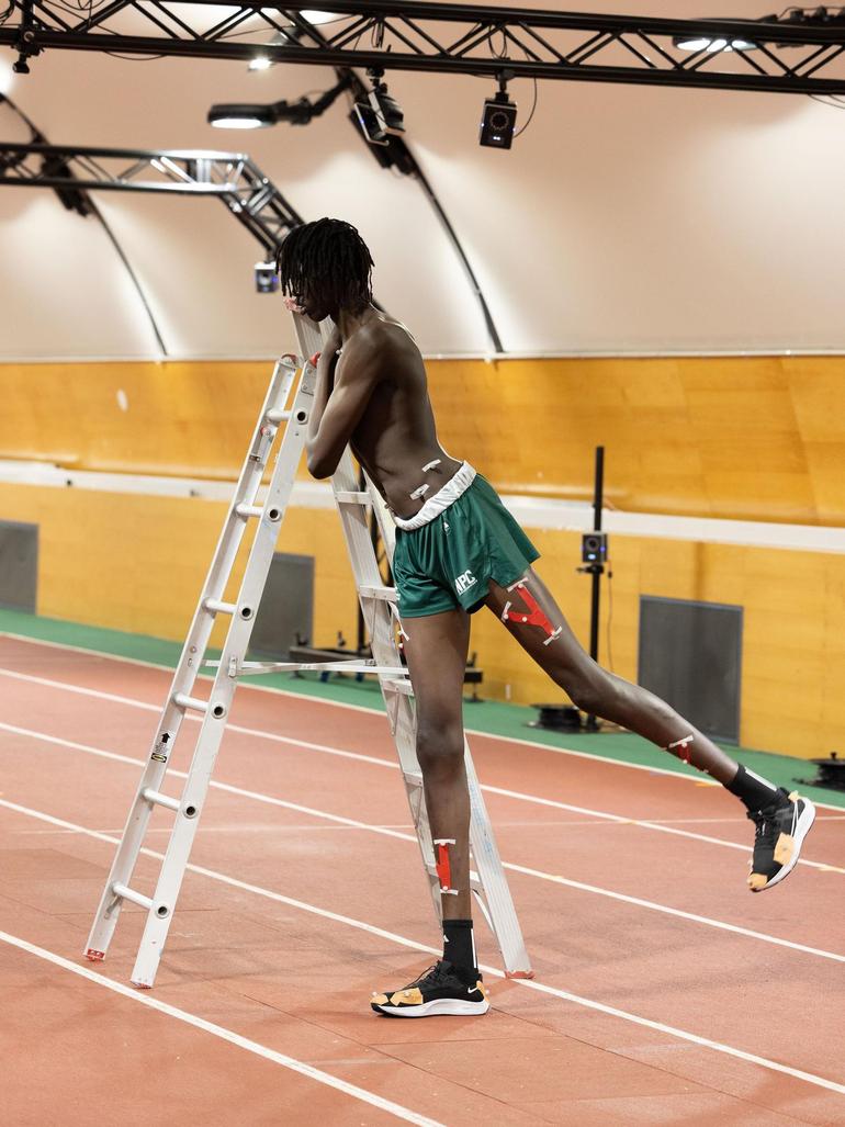 all basketball recruit Jongkuch Mach leaning on a silver stepladder to stretch his legs during a motion-capture athletic assessment.