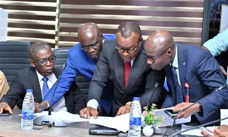 Government officials in suits reviewing legal paperwork and property bids at a conference table during the NDLEA asset disposal event.