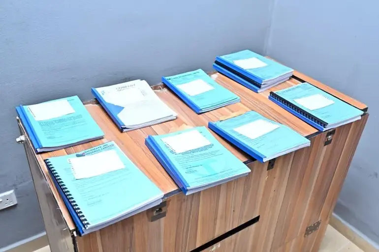 Several blue-covered official bid documents and property forfeiture files arranged neatly on a wooden desk.