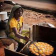 A woman sitting outdoors and frying golden-brown Akara balls in a large black pan filled with hot oil.