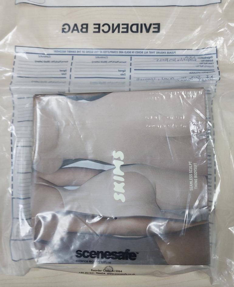 A box of Kim Kardashian's SKIMS Seamless Sculpt Thong Bodysuit shapewear packaged inside a clear plastic law enforcement evidence bag marked Scenesafe.